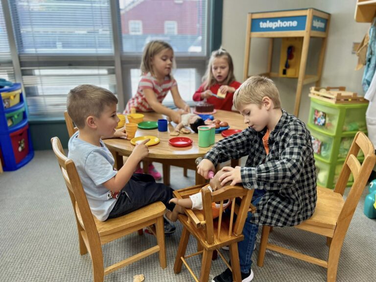 Photo of four preschool kids sitting at a table with a kitchen play set