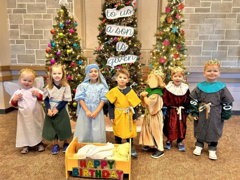 Photo of preschool kids dressed up for a Christmas pageant. Christmas trees in the background.