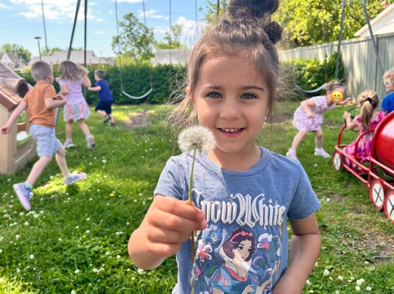 Close up photo of preschool kid giving dandelion flower to camera during recess